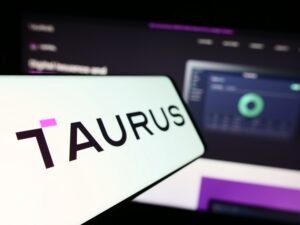 Smartphone avec logo de la société suisse d'actifs numériques Taurus SA sur écran en face du site internet de l'entreprise. Concentrez-vous sur la gauche de l'écran de téléphone. Photo non modifiée.