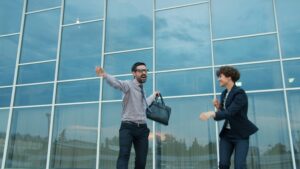 Group of happy businesspeople men and women are dancing outdoors near modern glass building in city street having fun together enjoying work success. People and celebration concept. Photo by Vitaly Gariev on Unsplash.