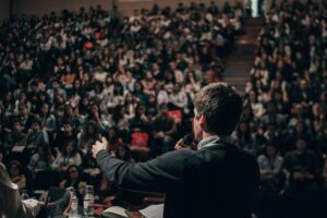Leader on stage, speaking in front of a crowd. Photo by Miguel Henriques on Unsplash